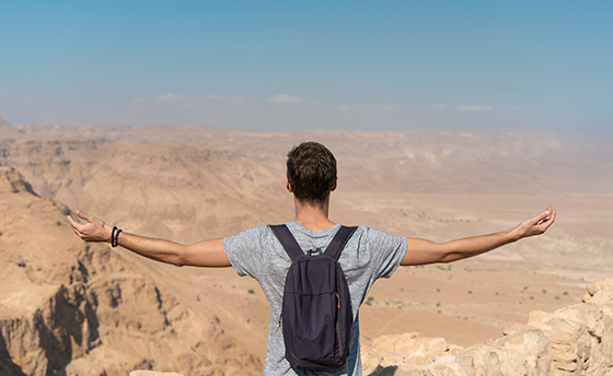 young man with arms raised looking the panorama over the desert in israel